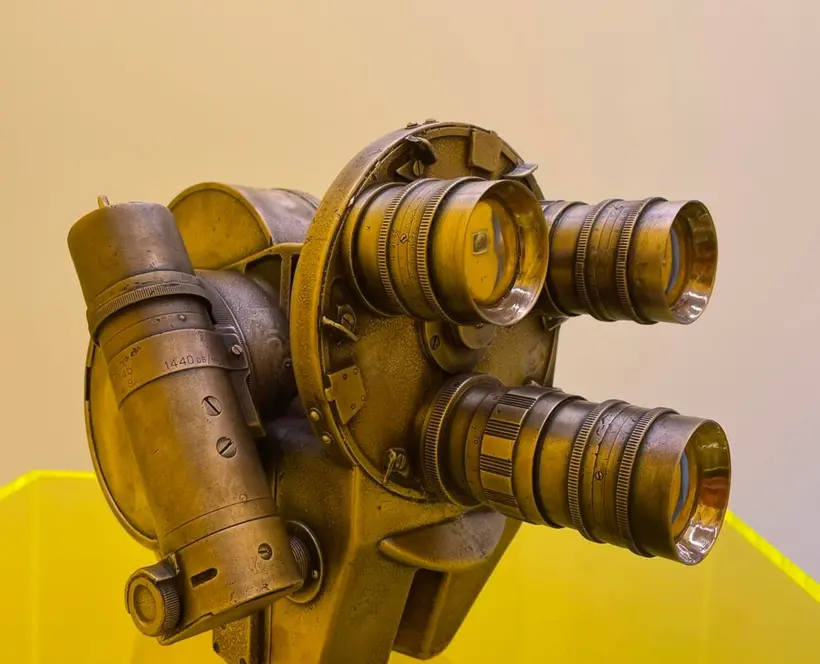 Image of old camera on yellow podium, the camera has three lenses, resembling a face or gas mask
