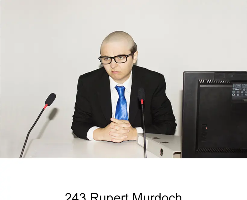 A person with no hair sat at a desk wearing a suit.