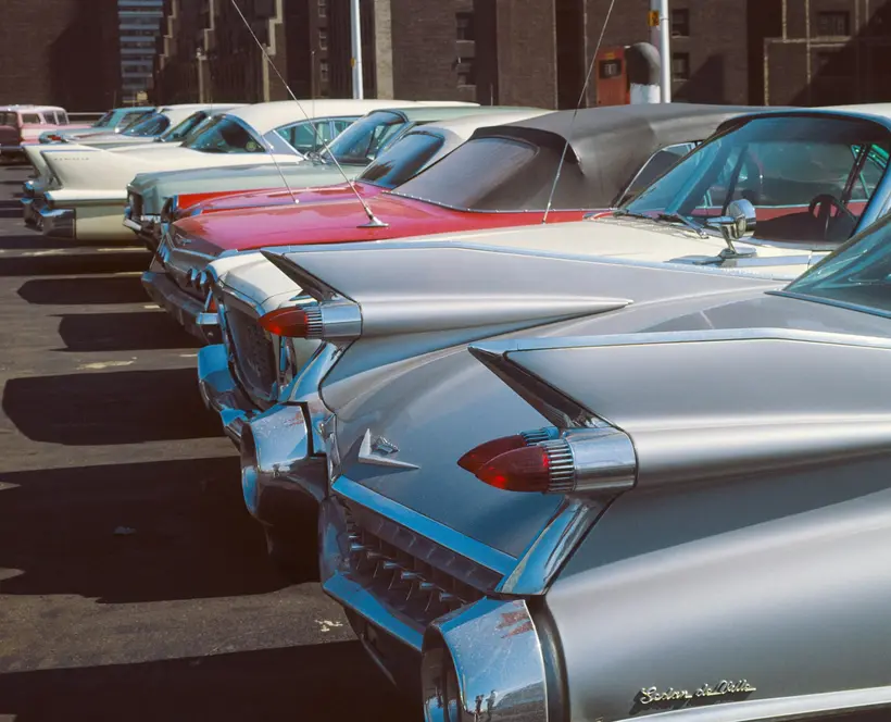 Colour photograph of a row of 1960s cars in a parking lot.