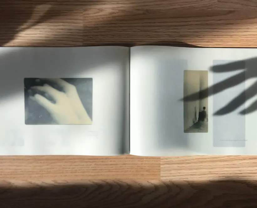 A photograph of a book laid out on a table with shadows of hands going across the page.
