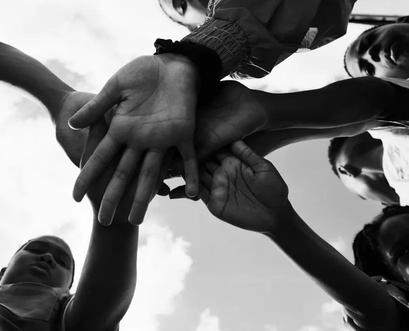 Black and white image taken from below of a group of four children with their hands in the middle, palms facing the camera