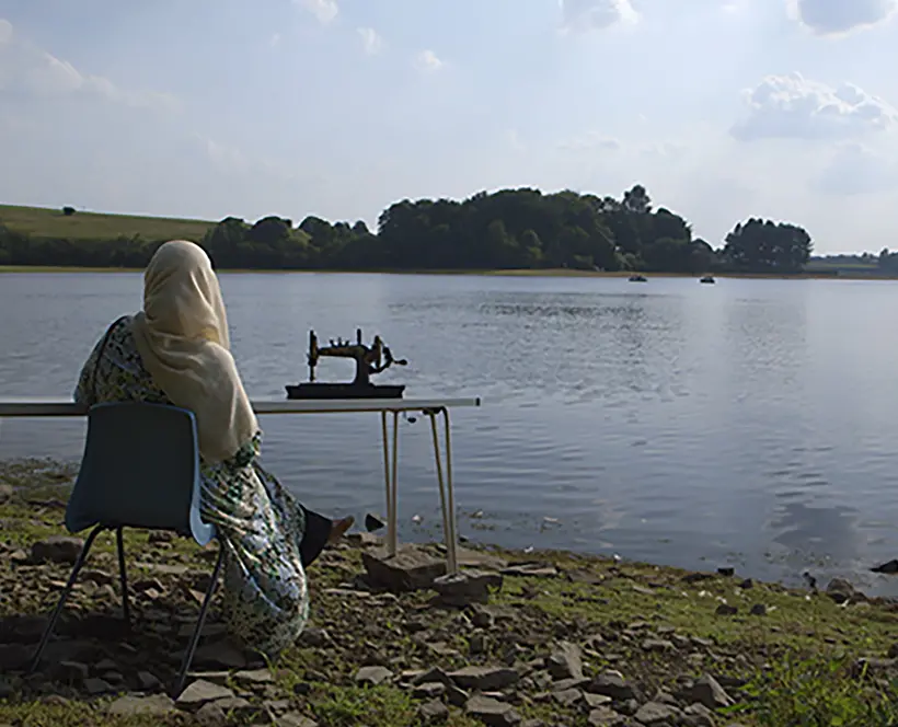 A woman sits overlooking a lake with a sewing machine