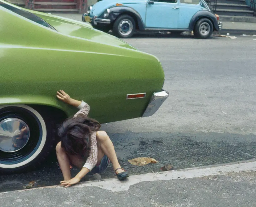 Child squatting looking under a green car