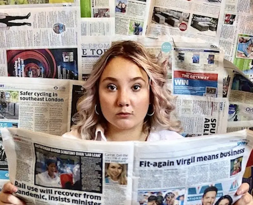 A photograph of a person surrounded by newspapers and reading a newspaper. 