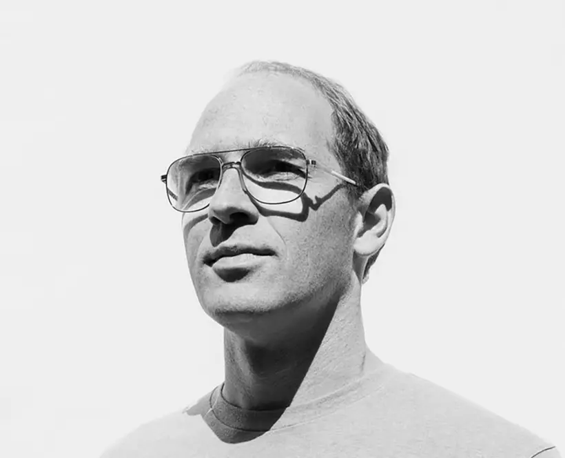 Black and white head and shoulders portrait of a white man wearing aviator style glasses looking off to the right smiling slightly.