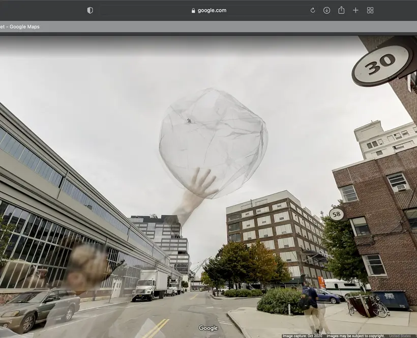 A screen capture of a person holding a balloon in front of a building on the side of a street on Google Street View