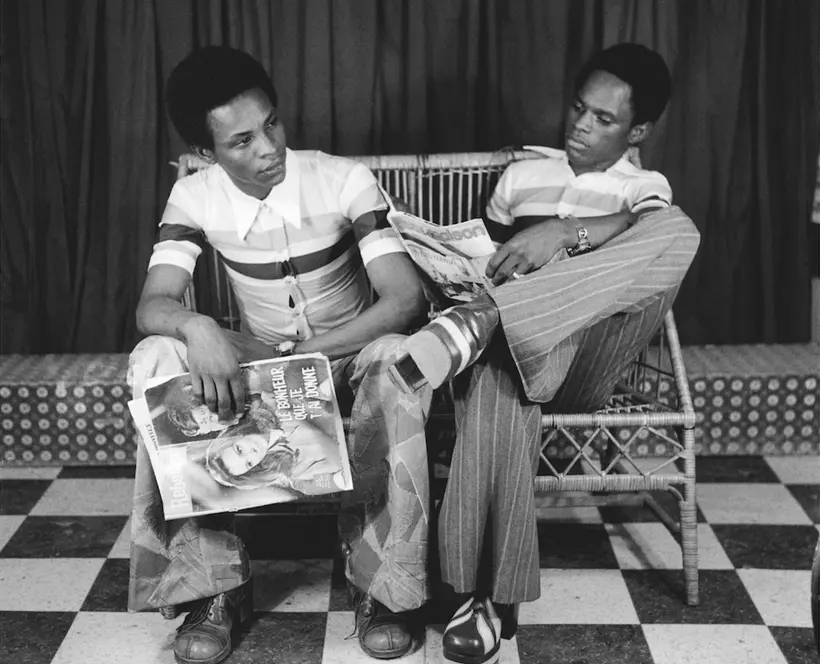 Black and white photo of two Black men seated on a bench in a studio portrait