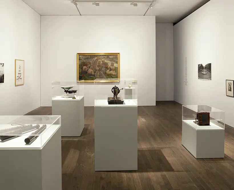 A white gallery room with objects on plinths and pictures on the walls.