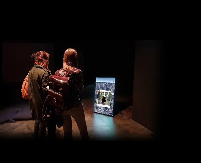 Two people looking at a screen on the floor on a dark exhibition space