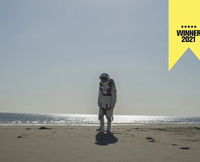 An astronaut stands alone on a beach