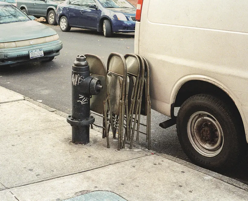 Street scene showing  a black fire hydrant and green chairs leaning a against a parked white van