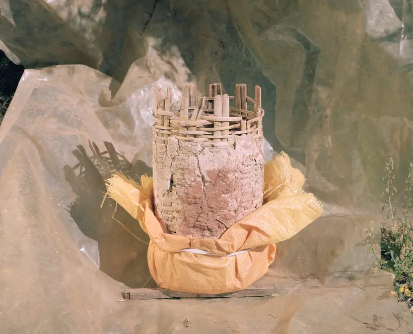 Cylindrical beehive made of sticks and mud half wrapped in a yellow plastic on a muddy plastic sheet photographed in the outdoors