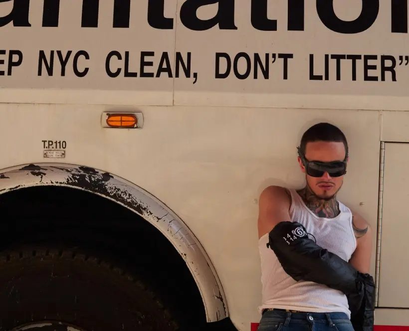 Colour photograph of a person sitting against the side of a vehicle with the words 'Keep NYC Clean, Don't Litter' on the side of the vehicle