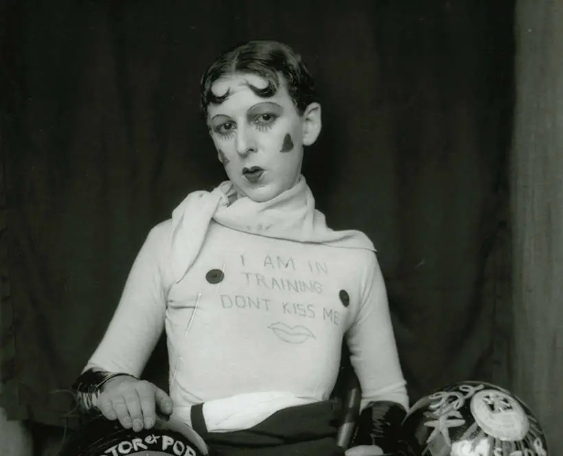 Black and White self-portrait of a Claude Cahun, sitting down wearing a white
