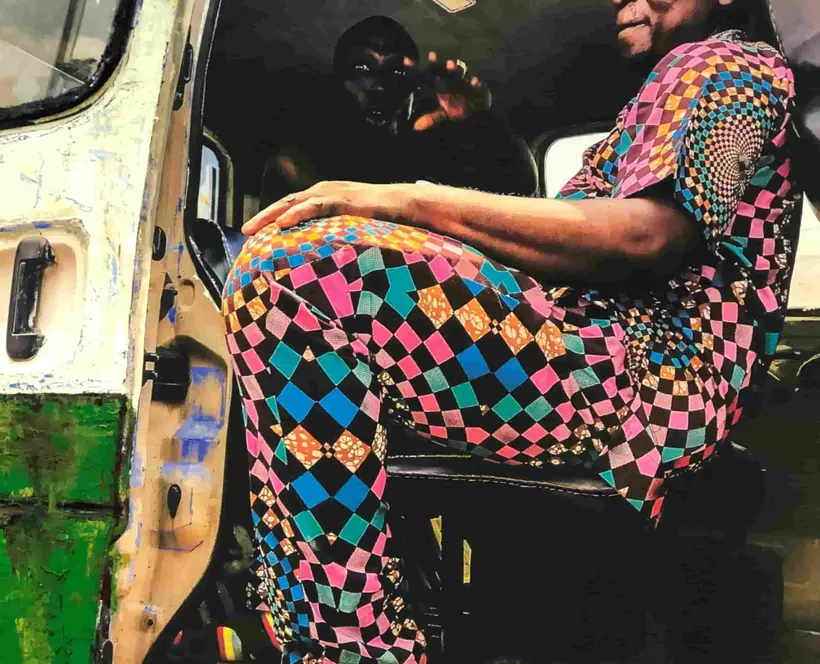 Two men sit in a bus, wearing colourful clothes. The image is overlayed with paint and embroidery 