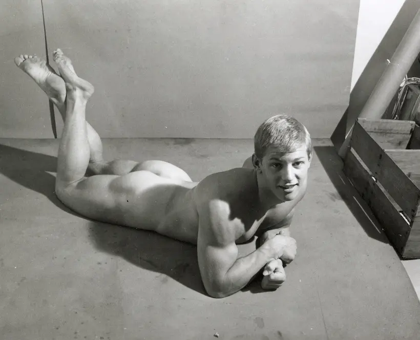 B&W photography of a white male figure laying on floor on stomach looking at camera