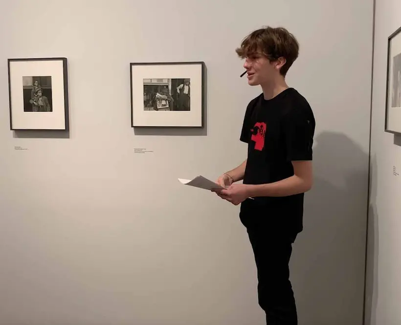a photograph of a person standing in front of photographs hanging on the wall.