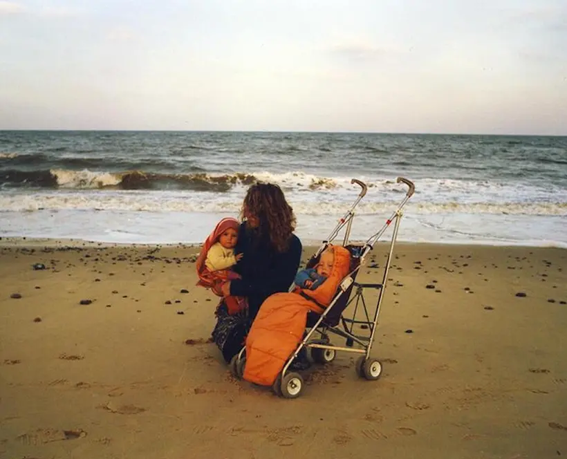 A picture of Jai Tyler's mother sitting on a beach, with Jai asleep in a pushchair, and holding Jasmine, Jai's oldest friend, in her arms.