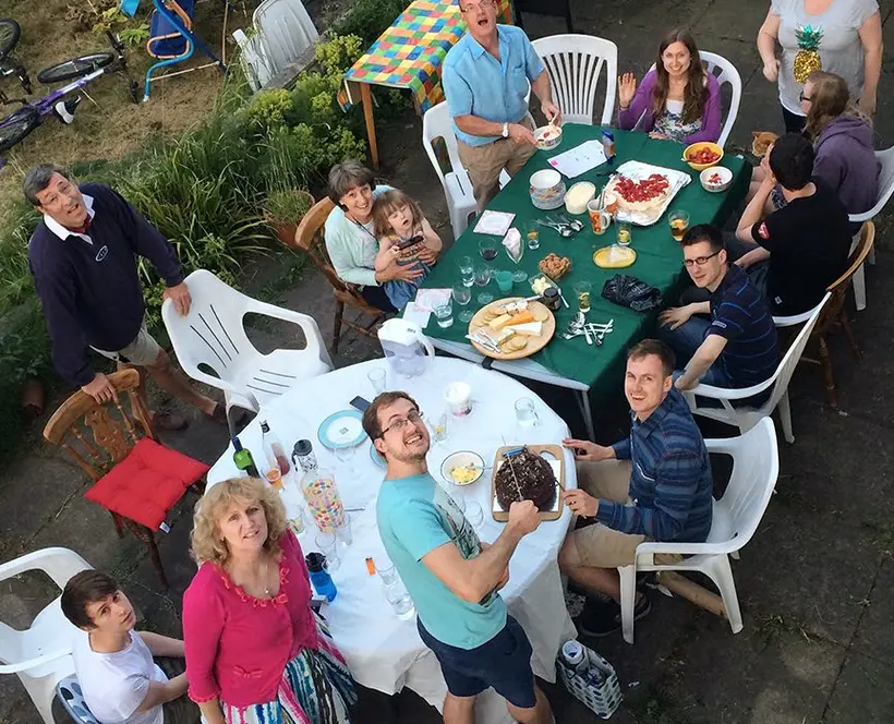 An image of a family gathered round a table for dinner in a garden