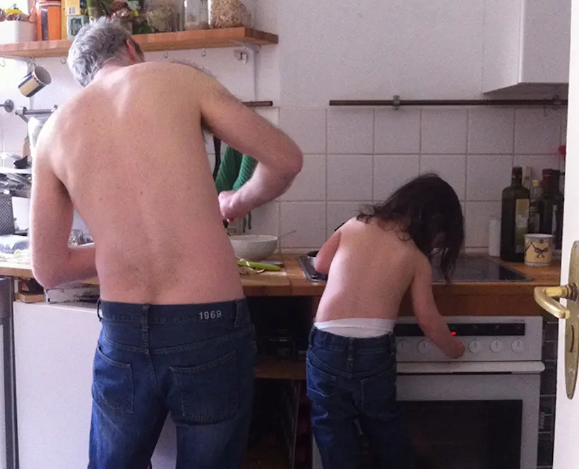 An image of a man cooking, accompanied by a little girl standing on a stall cooking next to him. Both are topless and wearing blue jeans.
