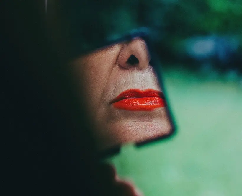A picture of a mirror with the reflection of an older woman's lips, wearing bright red lipstick
