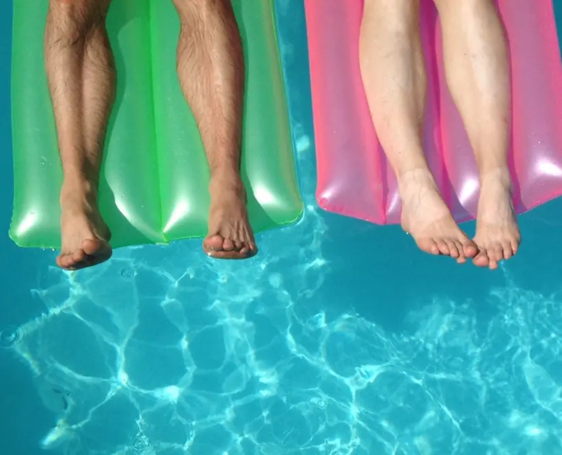A photograph of two sets of legs on lilo's in a swimming pool. One lilo is green, the other is pink.