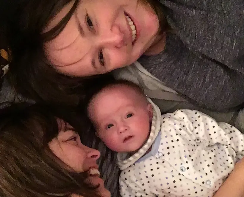 A picture of Holly Cocker, her wife Kate and their baby. All three of them are laying down together.